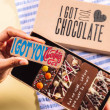 Hand holding a chocolate bar that reads “I Got You Chocolate” in front of an open gift box – a light-hearted and thoughtful apology gift.