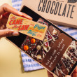 Hand holding a chocolate bar that reads “She came, she saw, she forgot why” in front of an open gift box – a humorous and thoughtful treat for menopause support.