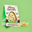 A white chocolate Easter egg with rainbow colours in a box, next to a stack of broken white chocolate Easter egg pieces