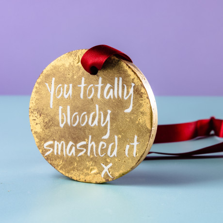 Close up of medal to detail gold lustre decoration and 'You totally bloody smashed it' slogan