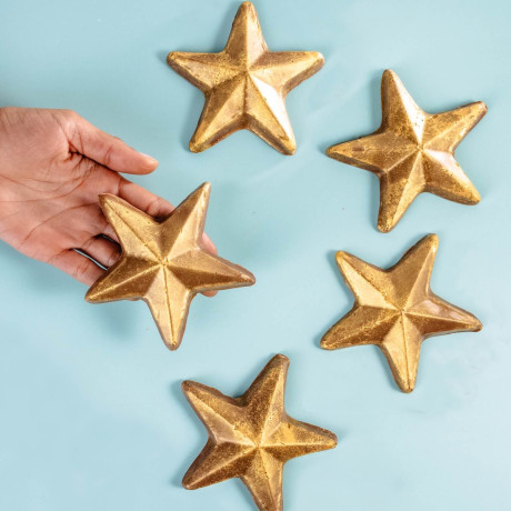 Five edible gold chocolate stars on a blue surface, with a hand reaching in – a fun twist on reward chocolate.