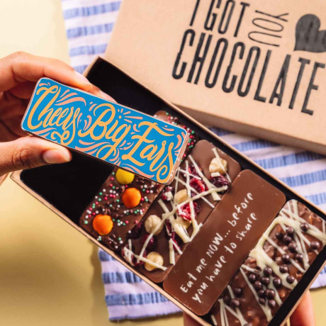 Hand holding a “Cheers Big Ears” chocolate bar above an open gift box of handmade bars – a fun way to say thanks with chocolate.